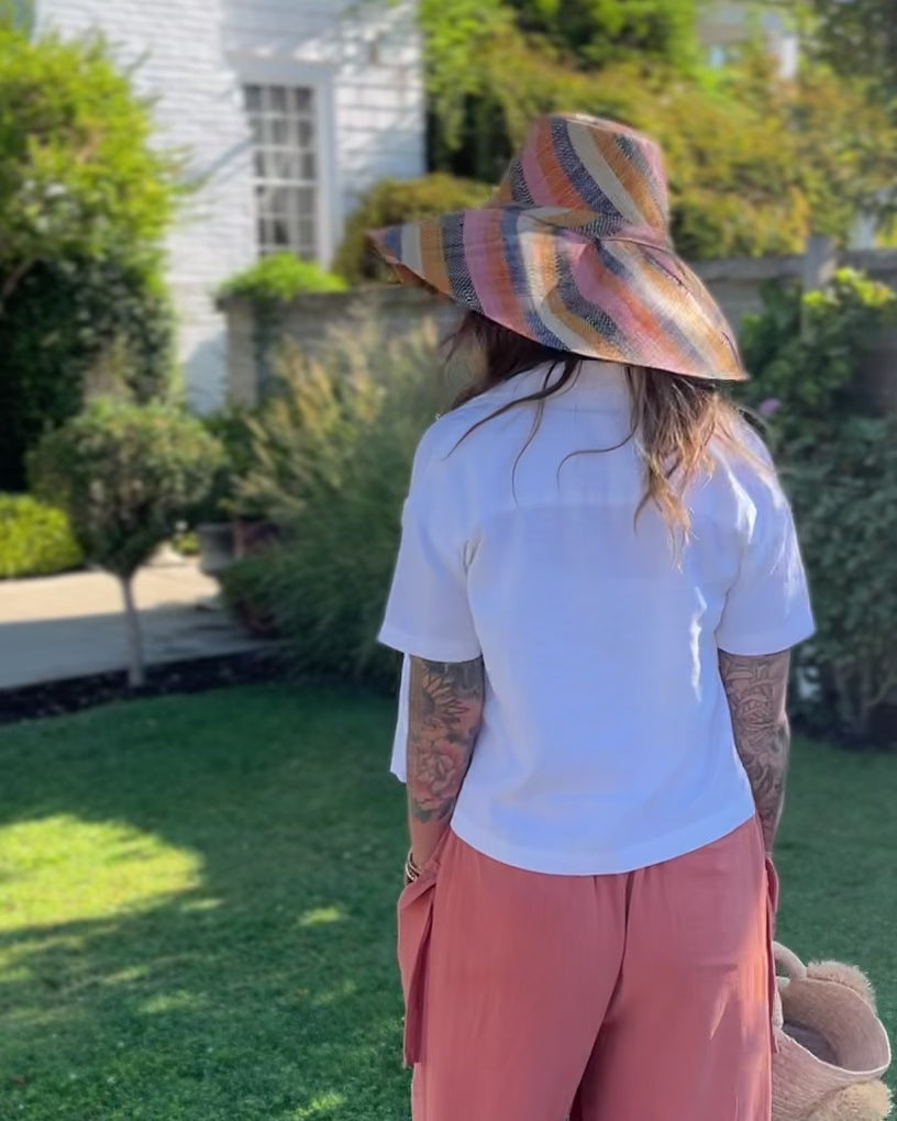 Model wearing Monica 7" Wide Brim Candyland Multicolor Stripes Packable Straw Sun Hat handmade loomed raffia in bands of natural straw color, black, saffron yellow/orange, light pink, coral orange/red, and dusk navy/dark/blue stripes create a swirl pattern - Shebobo