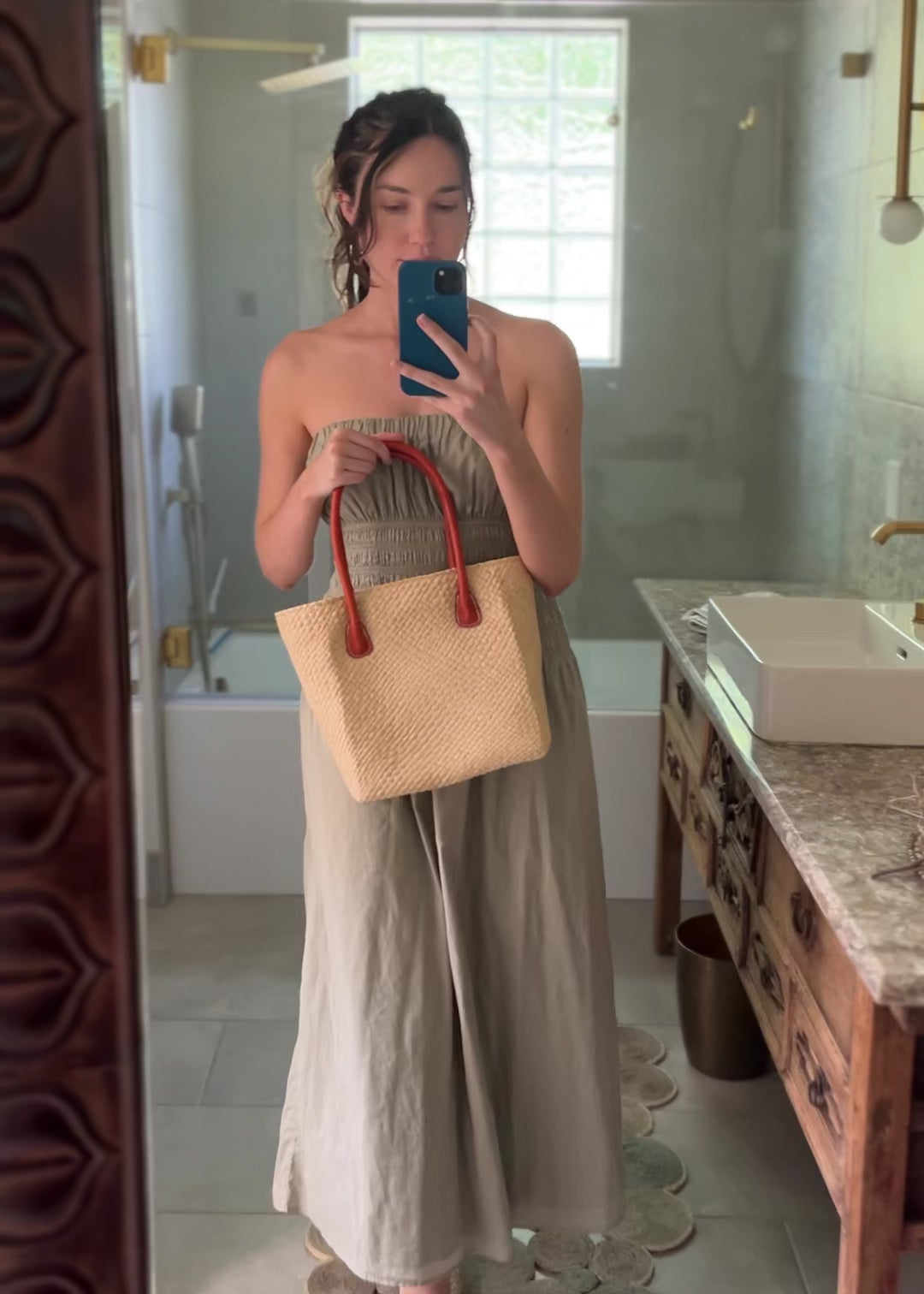 Model wearing Pianina Natural Small Straw Basket Bag handmade from woven natural raffia palm fiber in a monochromatic cross weave pattern of natural straw color handbag purse with leather handles - Shebobo