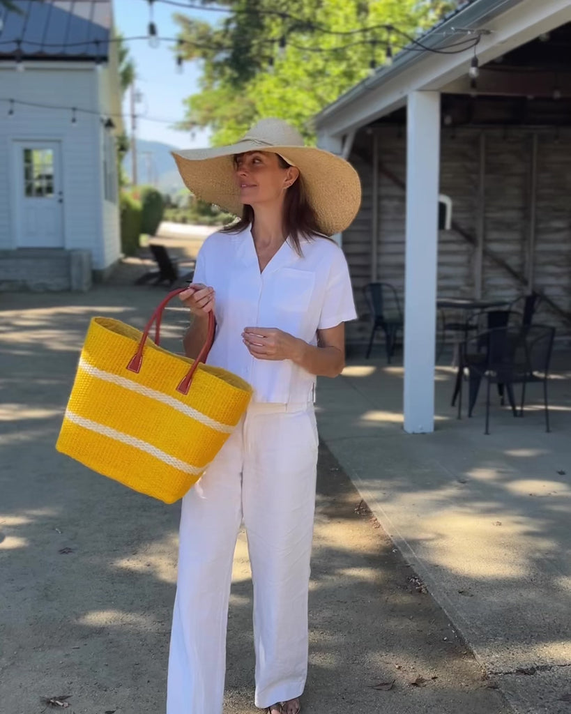 Model wearing Havana Sisal Basket Bag with Tassel Charm Embellishment handmade sisal fiber woven into horizontal wide bands of saffron yellow with two evenly spaced narrow bands of natural straw color create a stripe pattern with natural crochet starfish charm embellishment and leather handles handbag shoulder bag - Shebobo (with Natasha 7" Wide Brim Woven XL Straw Sun Hats)