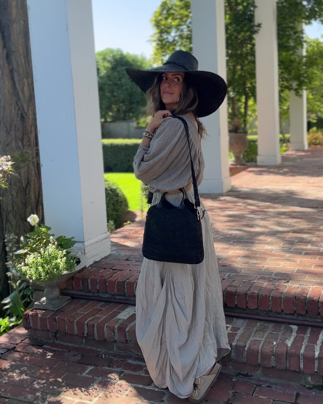 Model wearing Victoria Crochet Straw Handbag Convertible Crossbody Bag handmade crochet natural raffia palm fiber in a solid hue of black in a subtle texture of horizontal link bands pattern across the bag and m shape around the top of the bag with black leather handles and removable matching crossbody strap convertible purse - Shebobo (with Natasha 7" Wide Brim Woven XL Straw Sun Hats)