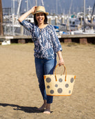 Model wearing Capri Polka Dot Grey Small Straw Tote Bag handmade loomed raffia palm fiber in a solid hue of natural straw color with various sized grey dots stitched on in a random pattern with leather handles and accents handbag shoulder bag beach bag - Shebobo (with Crochet Fedora Natural with Grey Band Unisex Straw Hat)