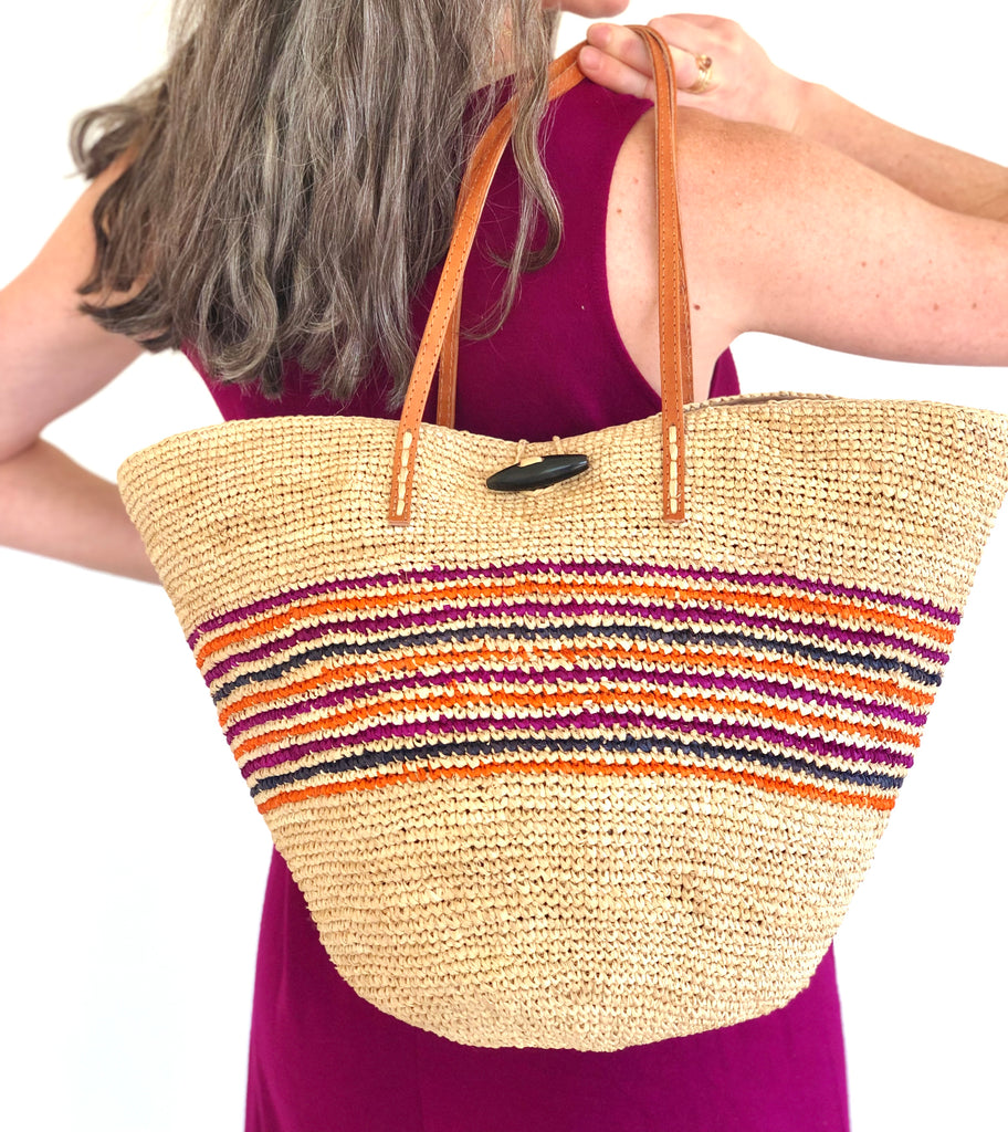 Model wearing Kerry crochet straw handbag handmade raffia natural with multicolor (fuchsia pink, coral orange, and navy blue) horizontal pinstripe pattern mid bag purse with leather handles beach bag - Shebobo
