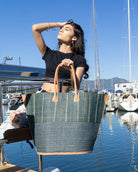 model wearing Santa Cruz Two Tone Large Straw Tote Bag handmade beach bag loomed raffia solid grey bottom with grey and natural vertical pinstripe pattern top plus leather handles xl handbag - Shebobo